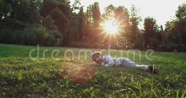 有魅力的小男孩两岁，摔倒在绿草上，直视着镜头，笑得很可爱